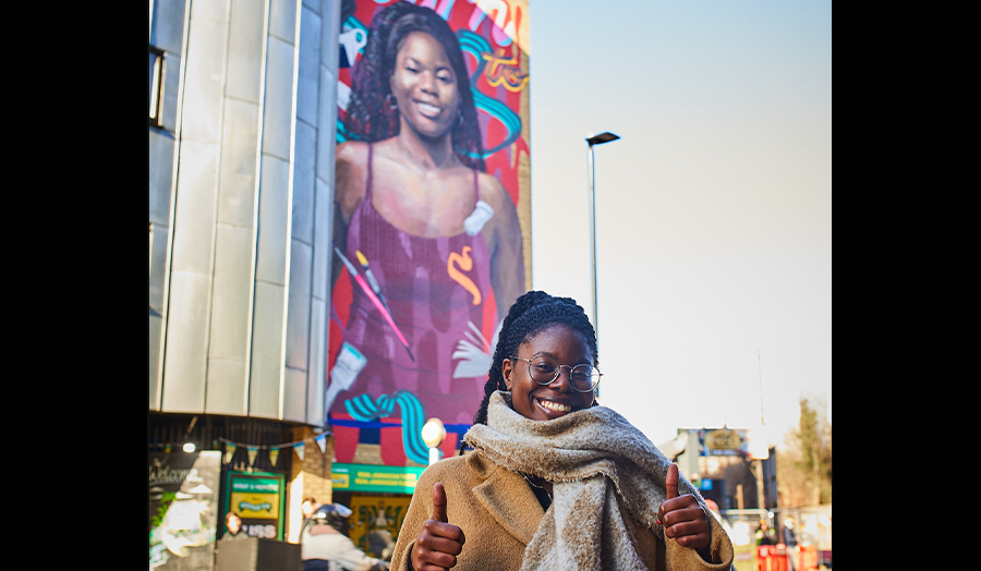 Graduate Maria standing in front of a mural depicting her